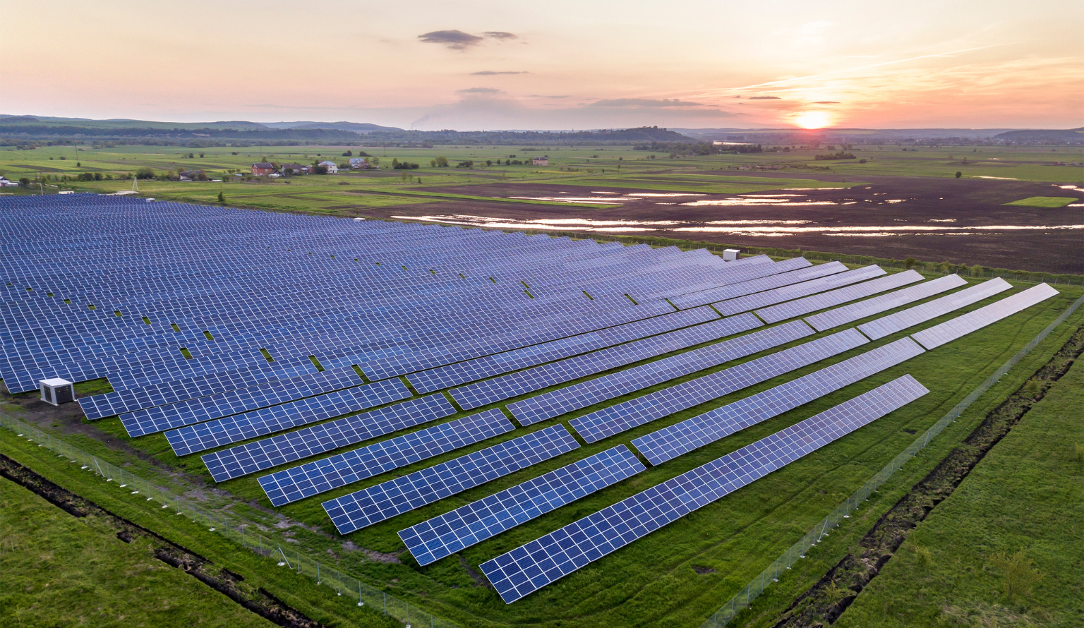Large solar power plant with rows of photovoltaic panels in rural landscape at sunset