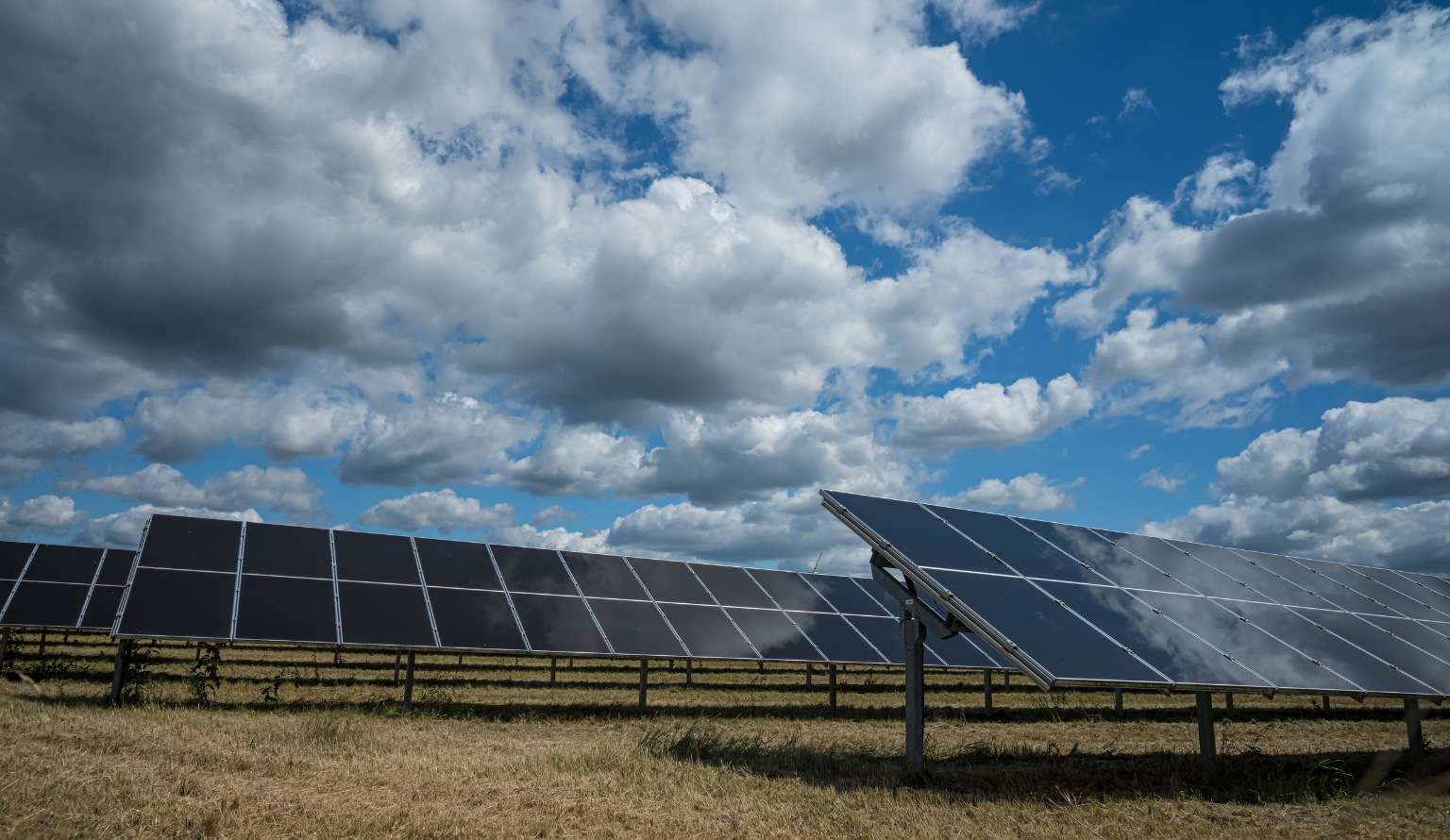 Solar panels in an open field generating renewable energy under a partly cloudy sky
