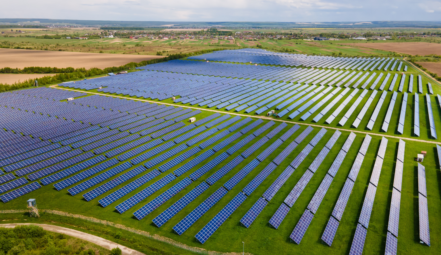 Large-scale solar power plant with rows of photovoltaic panels installed across green farmland in India